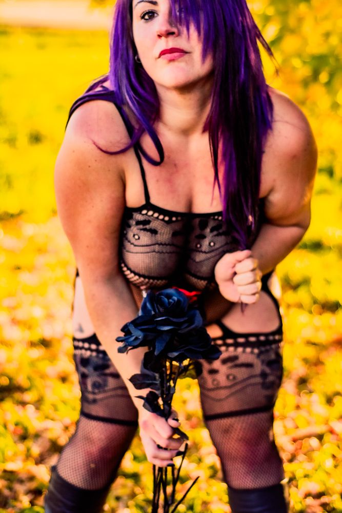 Figure in black lace lingerie holding blue roses against autumn yellow background.