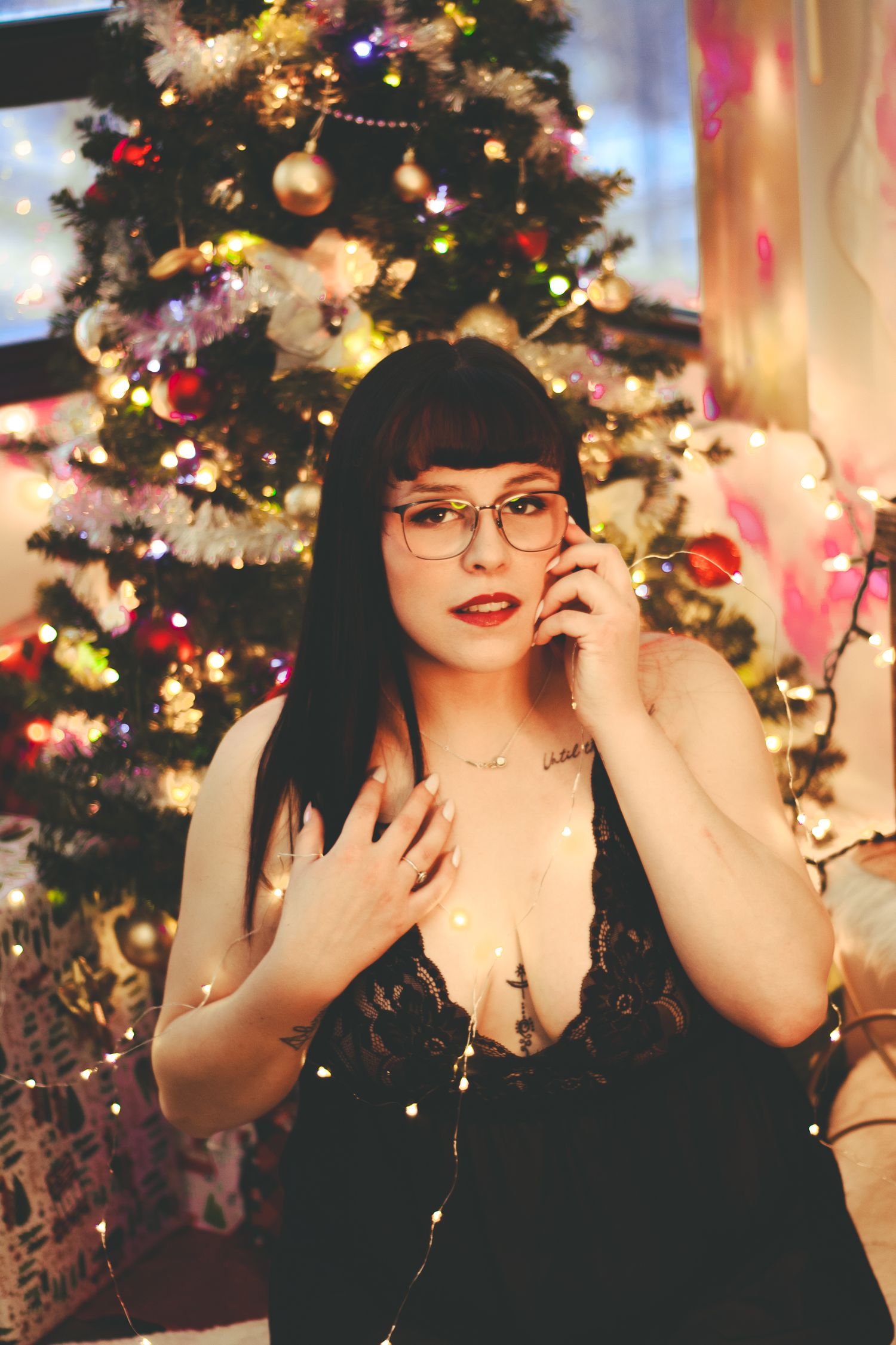 Festive holiday photoshoot with decorated Christmas tree, string lights and ornaments in cozy indoor setting.