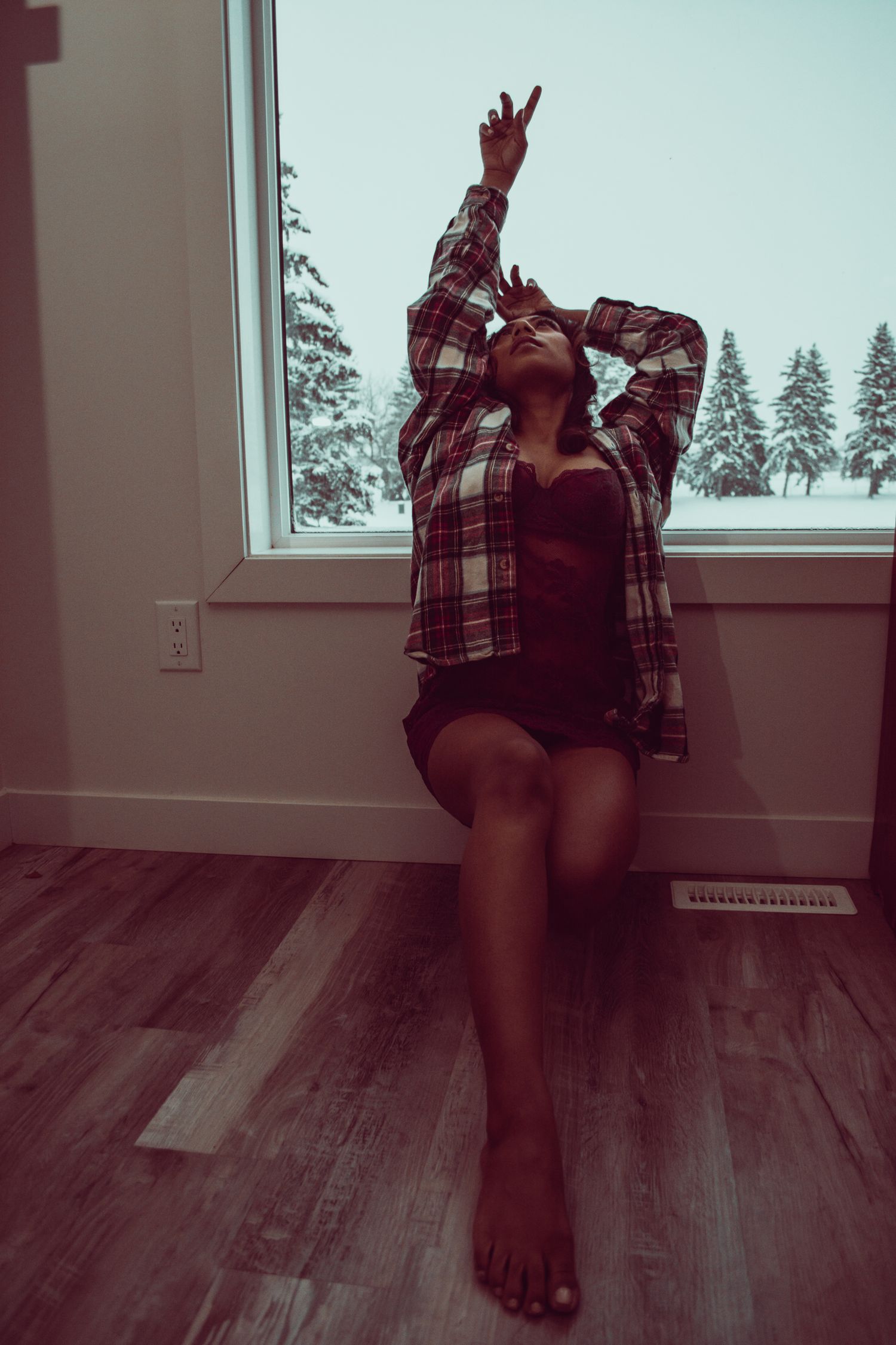 Artistic indoor photo with person sitting on floor reaching upward by window.
