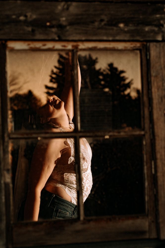 Dramatic pose captured through rustic window frame at golden hour.