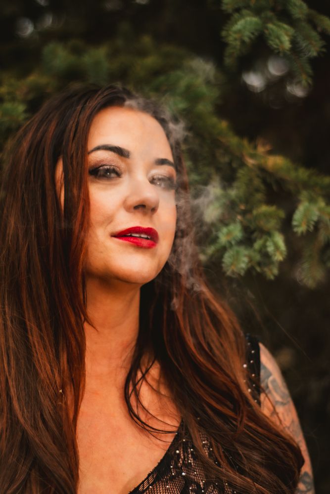 Close-up portrait with red lipstick and smoke effects in forest setting.
