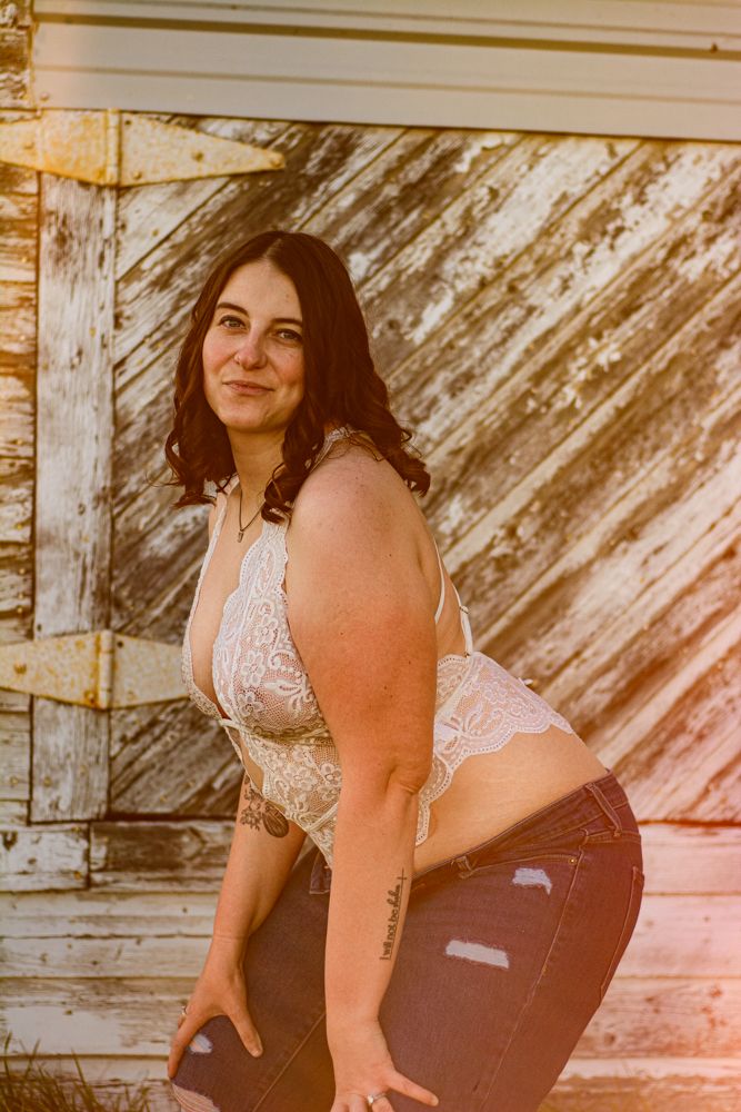 Artistic boudoir photo with warm sunset lighting against weathered wood siding.