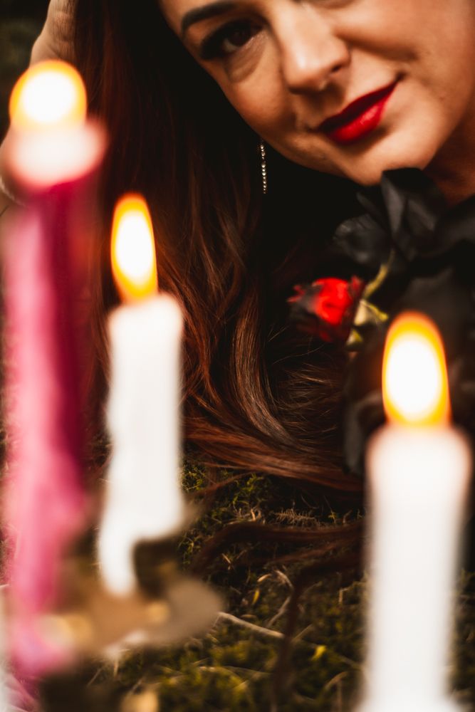 Atmospheric shot of lit candles with blurred person wearing red lipstick in dark setting.