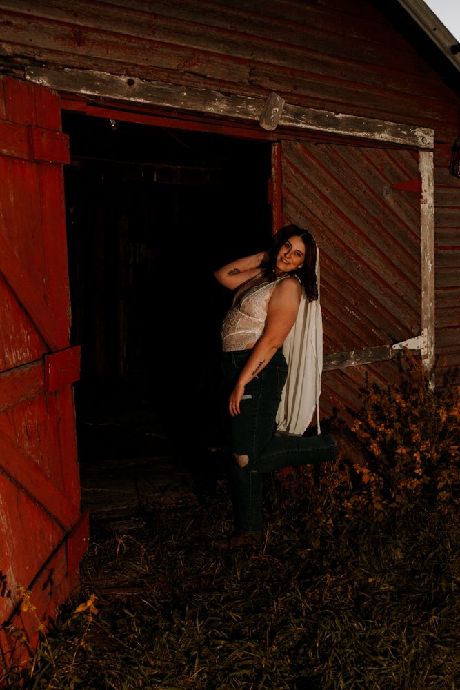 Dramatic pose in barn doorway with flowing fabric and natural evening lighting.