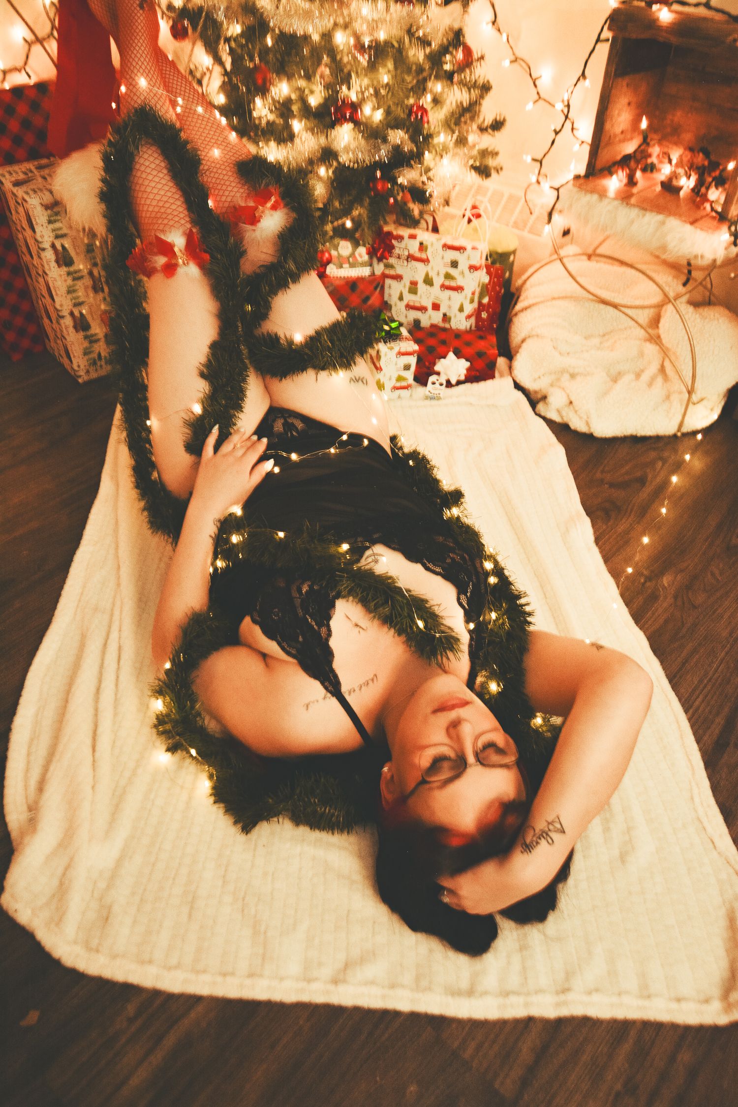 Holiday boudoir photography with black lace and feathers against festive Christmas backdrop.