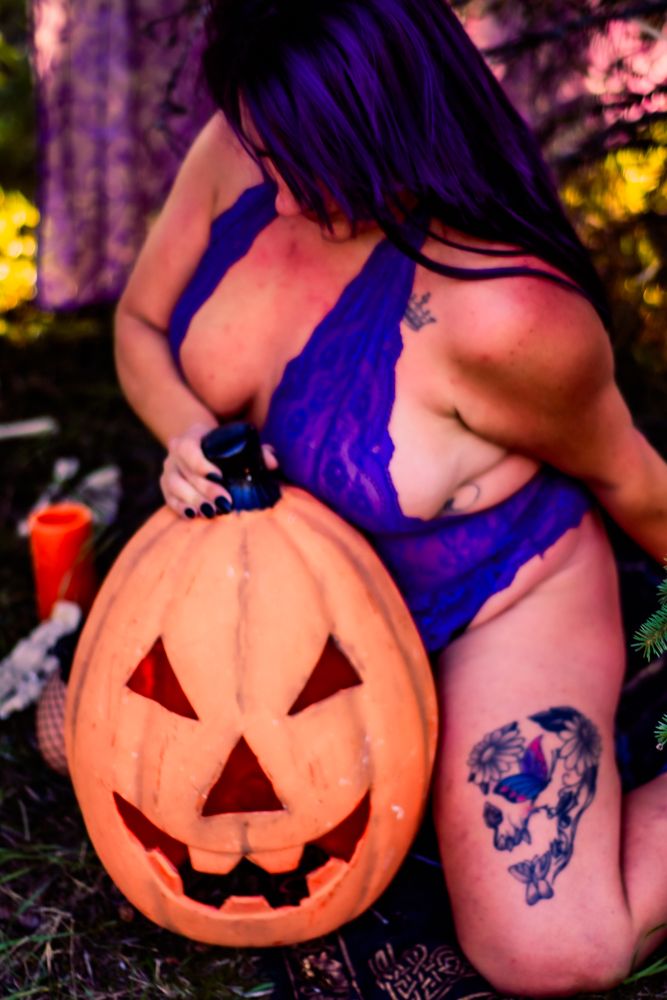 Halloween boudoir photo featuring carved pumpkin and purple lace costume with gothic decorations.