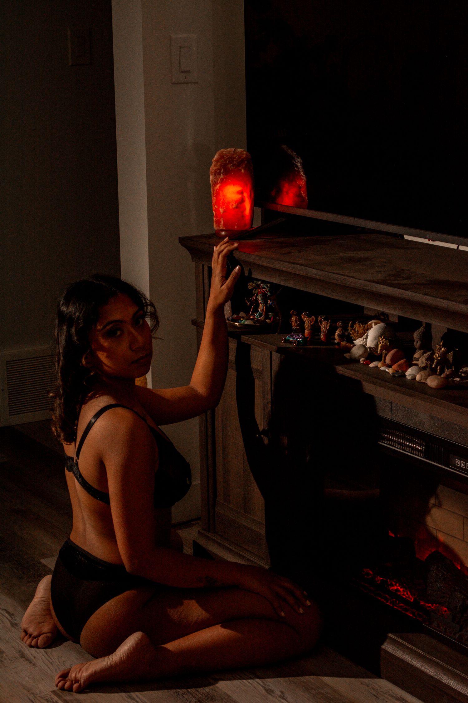 Dimly lit indoor portrait with red lanterns and an electric fireplace creating atmospheric lighting.