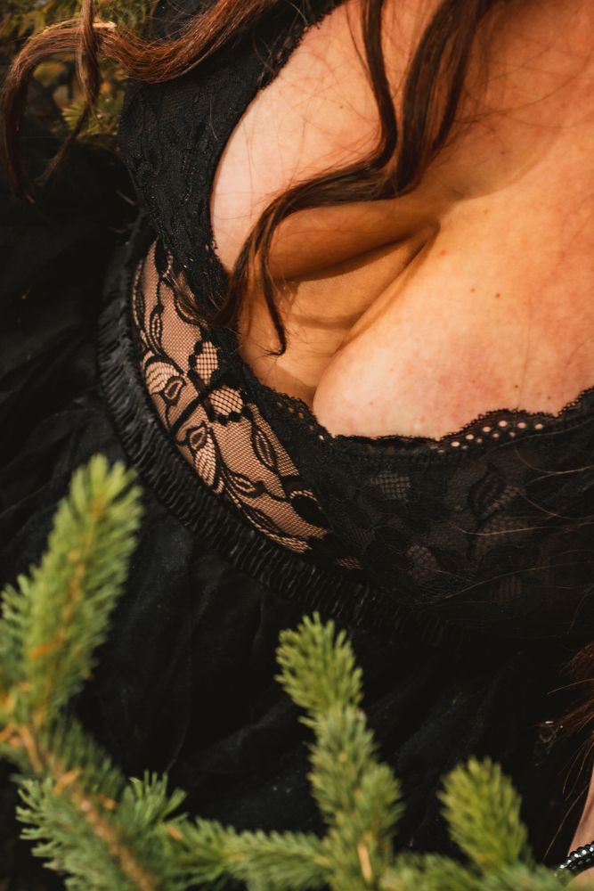 Detailed shot of black lace trim on clothing with evergreen sprigs in the background.