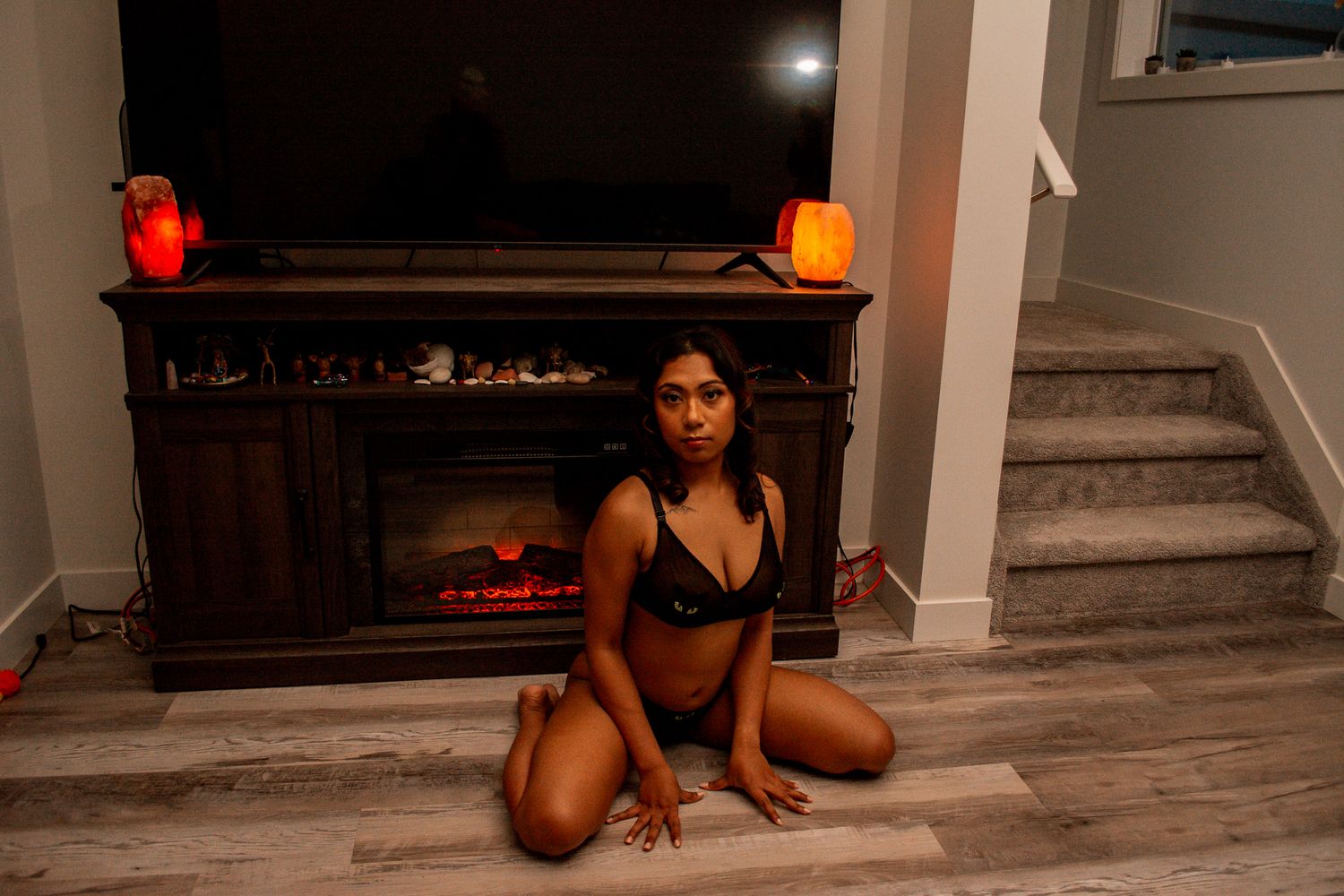 Intimate portrait in black lingerie by fireplace with glowing red and orange candles.