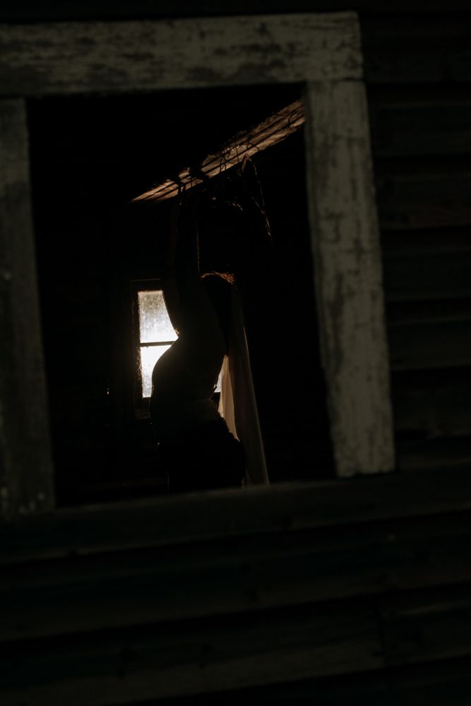 Silhouetted figure in a dark window frame illuminated by soft rays of light.