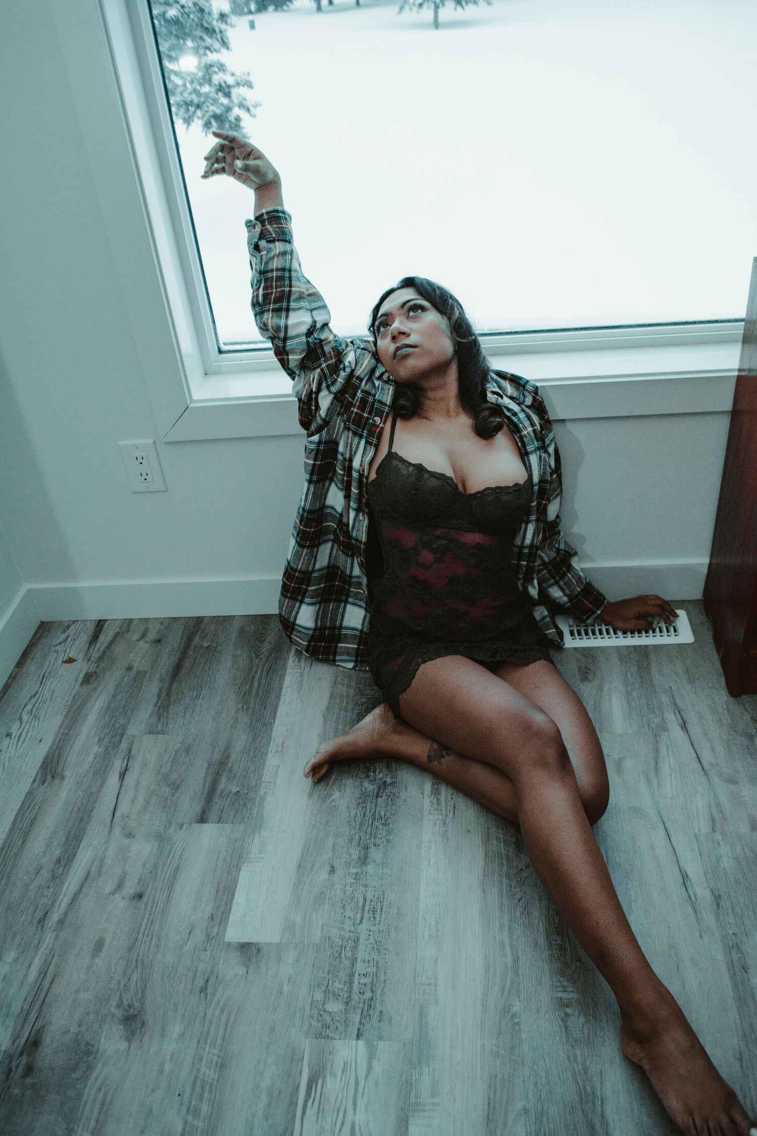 Person in plaid shirt posing artistically on gray wood floor with snow scene outside.