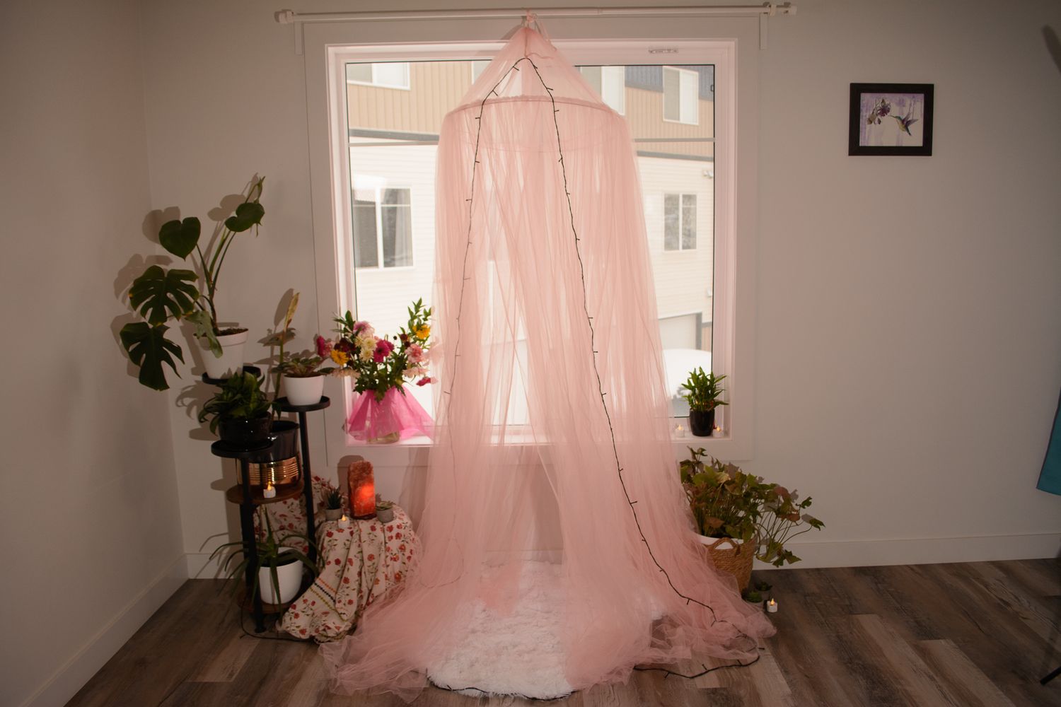 Pink canopy setup with flowers and plants creates romantic boudoir photography setting.