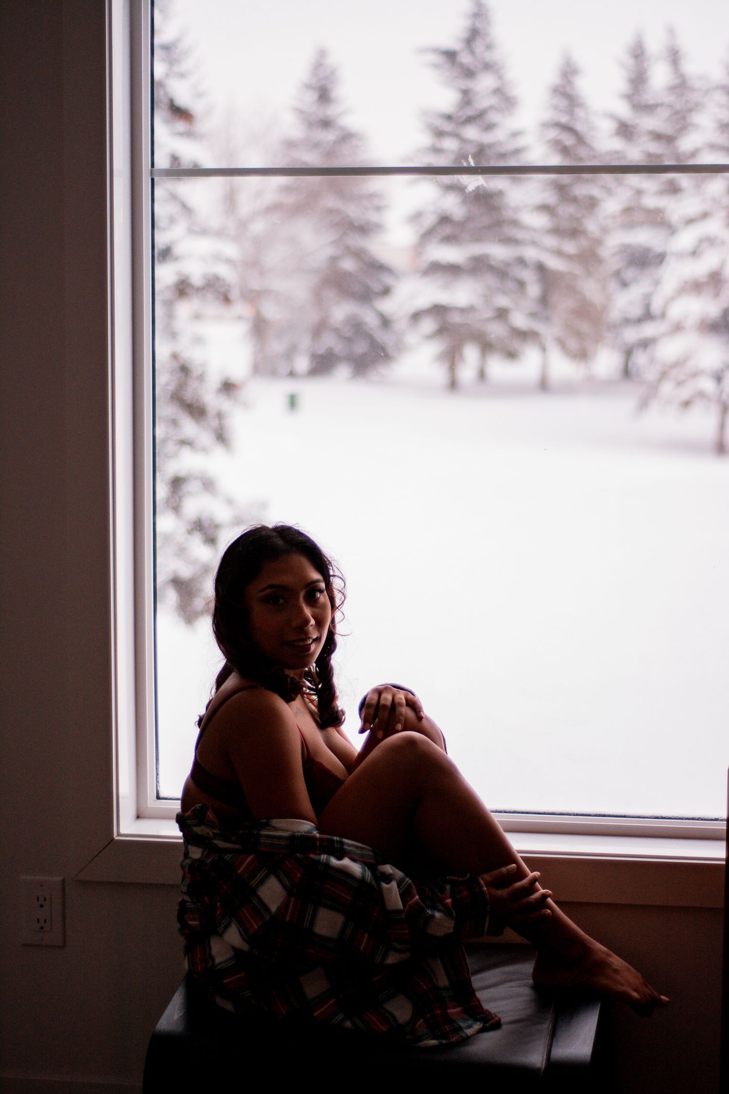 Intimate winter portrait by window overlooking snowy forest scene.