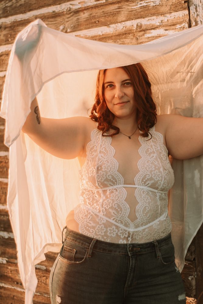 Boudoir style portrait against rustic wooden wall with warm sunset lighting.