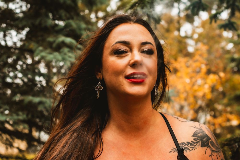 Outdoor portrait in autumn setting showing long dark hair and natural makeup against evergreen trees.