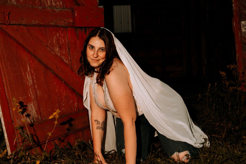 Artistic pose with flowing veil against rustic red barn door backdrop.