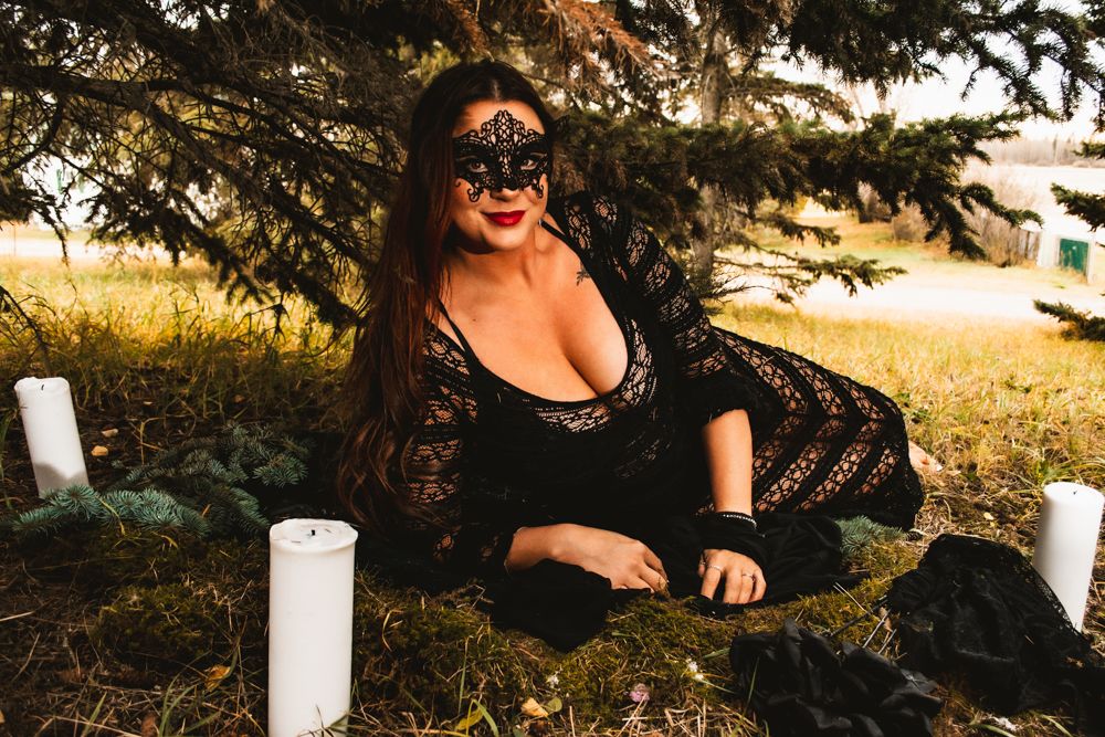 Gothic-styled outdoor photo with lace dress, mask and decorative white candles.