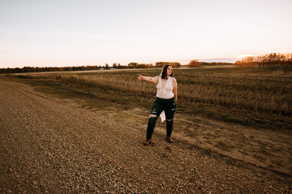 Person standing confidently on a dirt road surrounded by autumn fields at dusk.