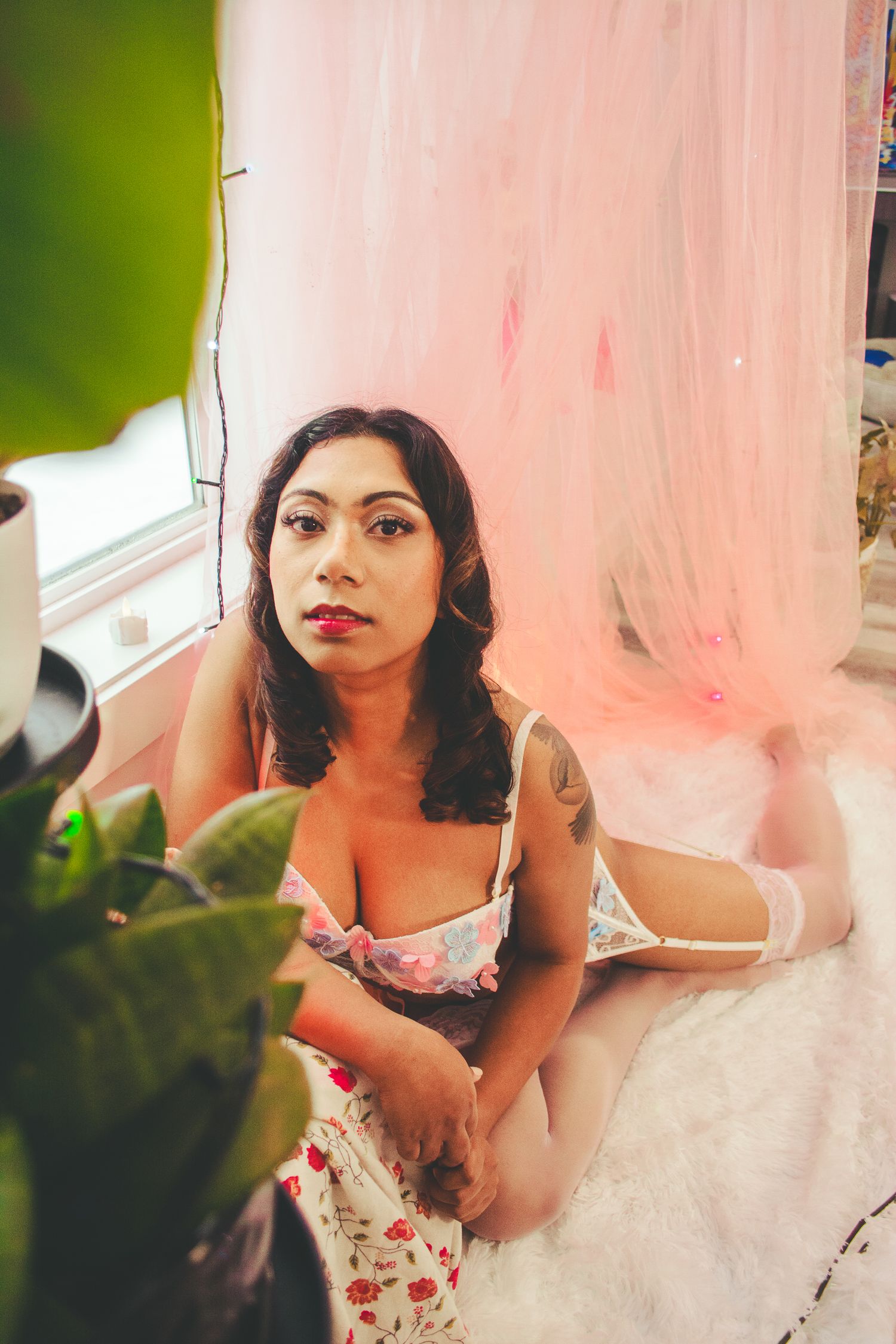 Artistic boudoir photography with houseplants and pink drapery creating a romantic atmosphere.
