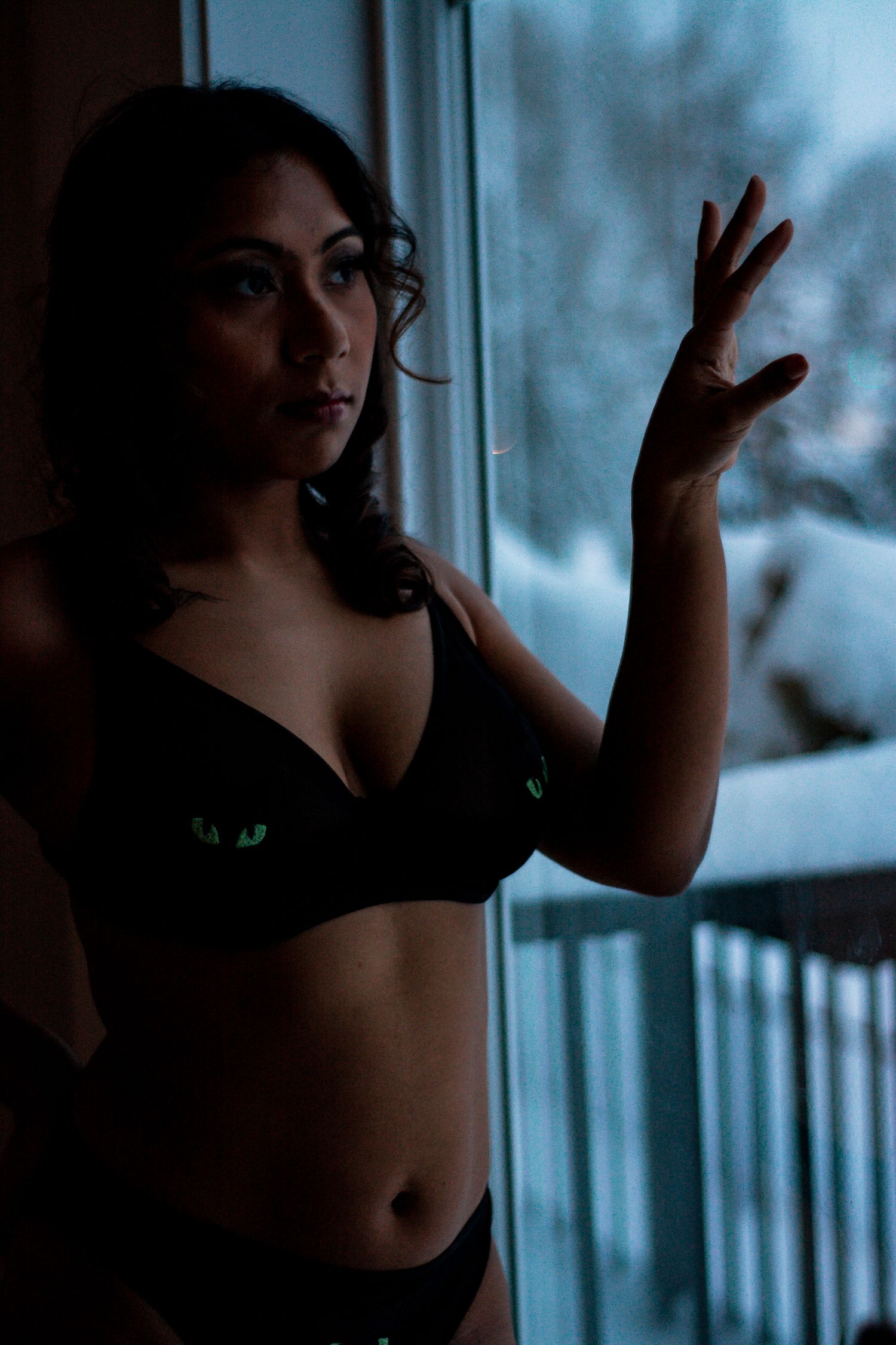 Figure in black lingerie poses artistically by window with snowy scene outside.