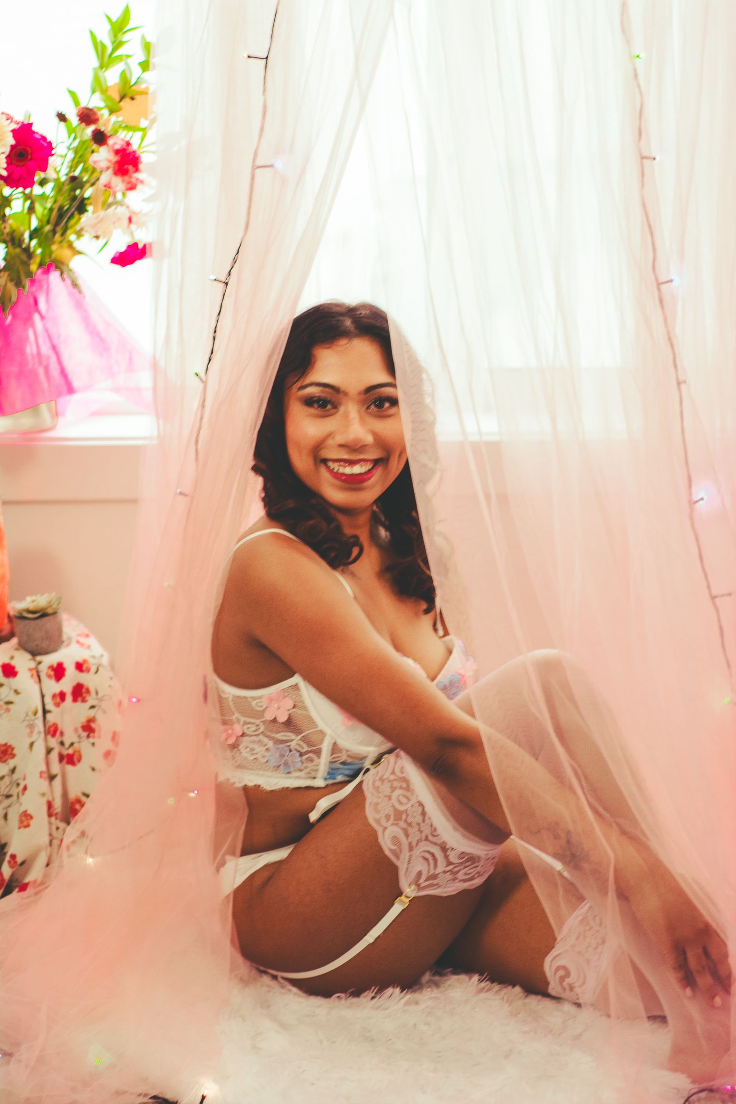 Boudoir photography session with pink curtains and floral decorations.