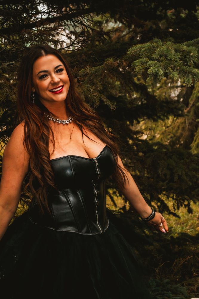 Dark romantic portrait with leather corset and tulle skirt against pine trees.