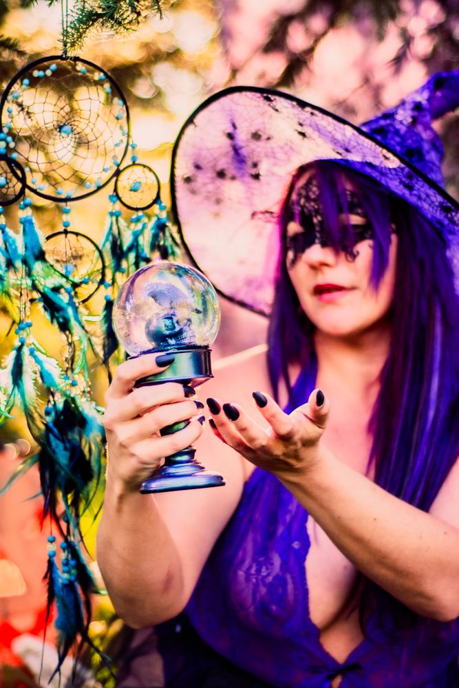 Magical Halloween scene with crystal ball, dreamcatchers, and purple witch attire against sunset lighting.