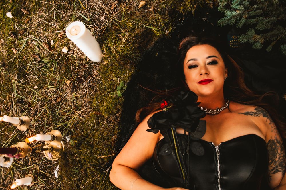 Dramatic outdoor portrait with black corset dress and floating candles in natural setting.