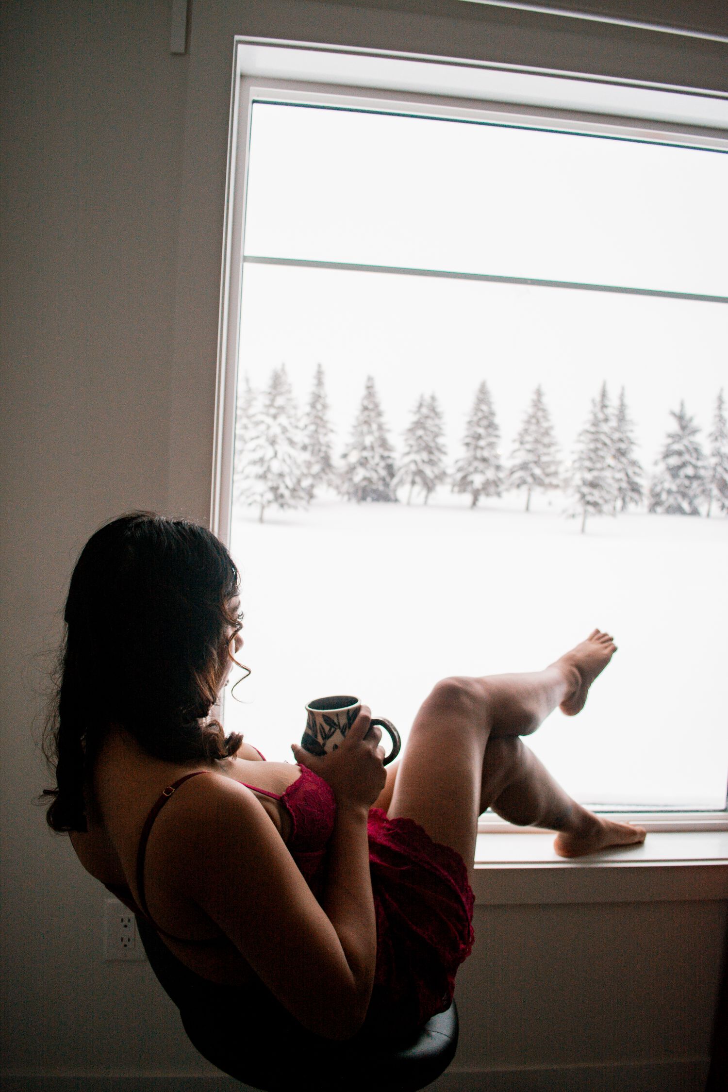 Woman relaxing by window with coffee cup overlooking snowy winter landscape.