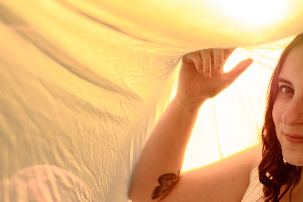 Soft sunlit portrait through sheer fabric creating an ethereal golden glow effect.