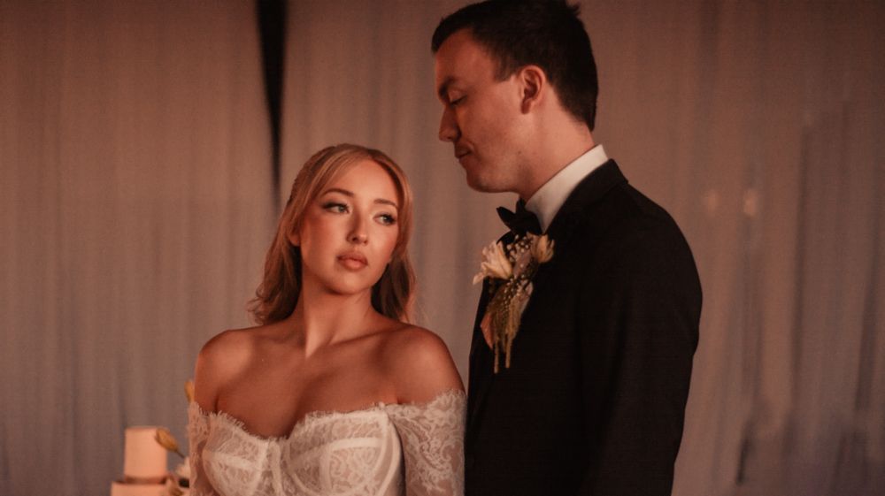 Intimate wedding portrait in warm lighting with classic black tuxedo and lace dress.