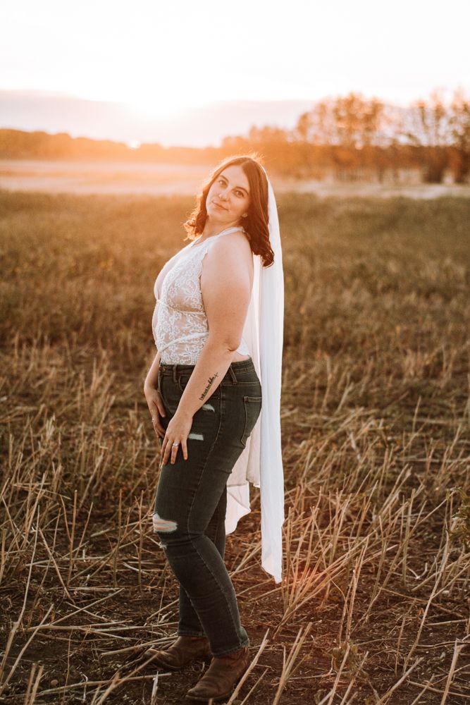 Person in lace top and jeans poses in field at sunset with flowing white fabric.