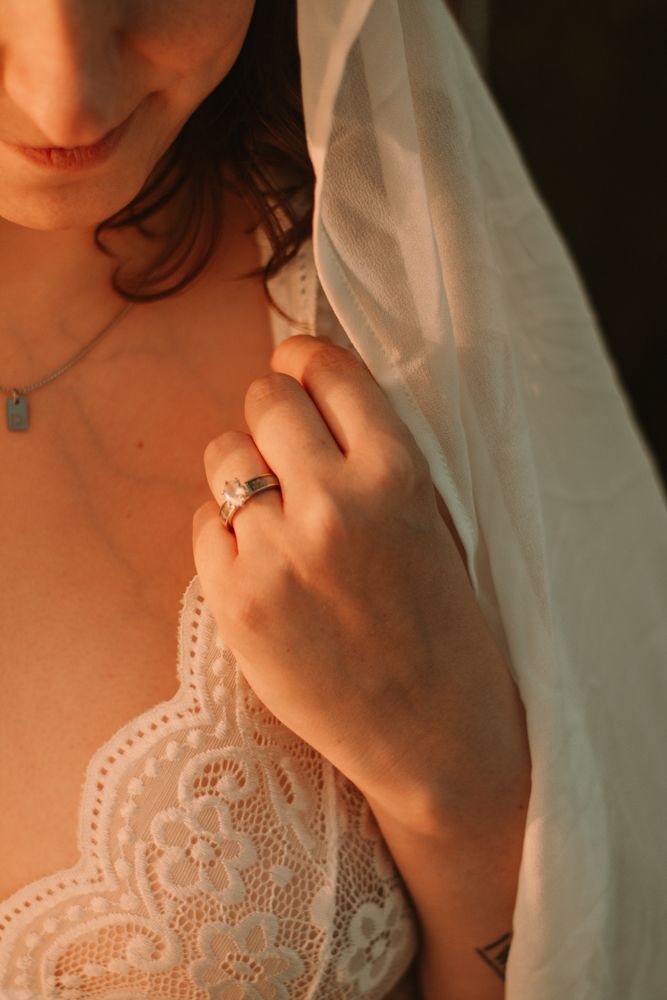 Detail shot of lace wedding dress bodice with engagement ring and veil.