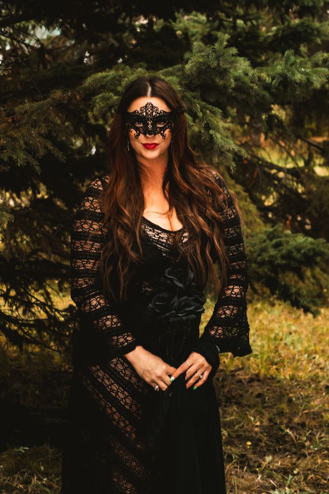 Gothic fashion portrait with intricate mask and lace dress in forest setting.