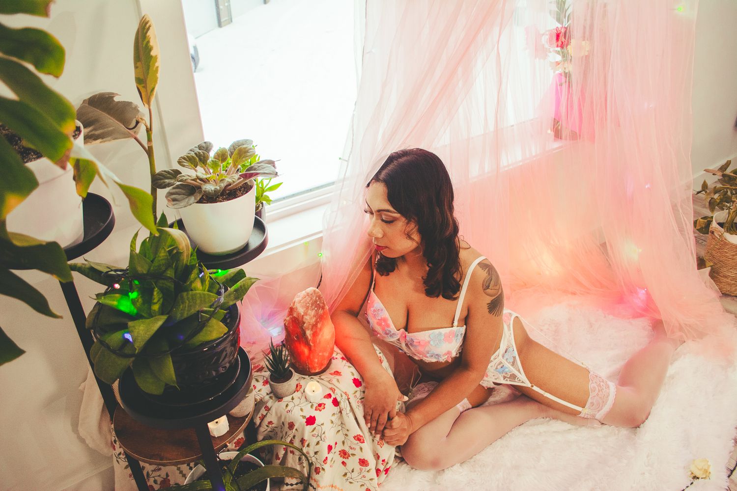 Intimate portrait in a dreamy pink room with potted plants and soft lighting.