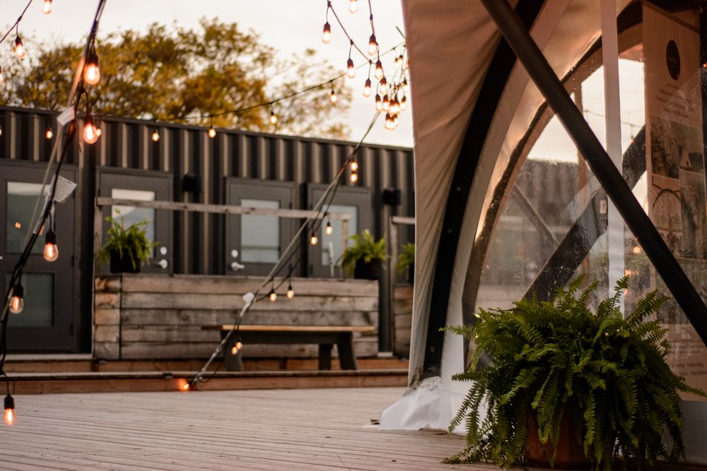 Outdoor venue decorated with string lights and greenery at dusk.