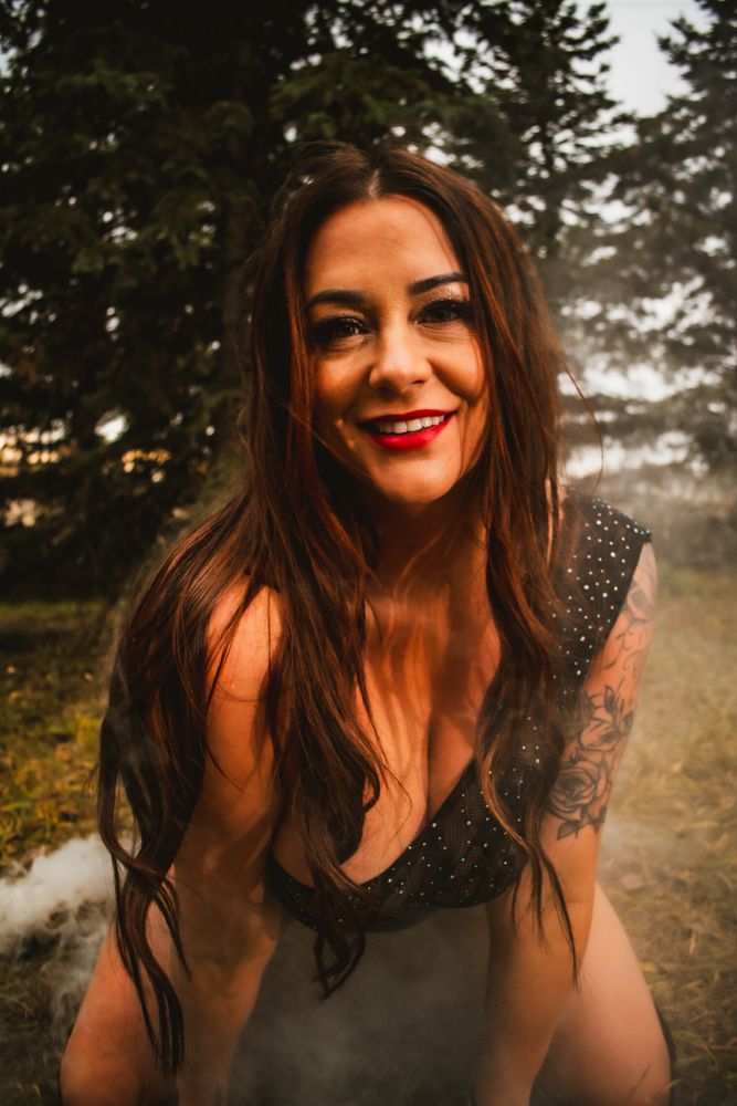 Woman in dark sparkly top poses outdoors with trees in background and a bright red lip color.