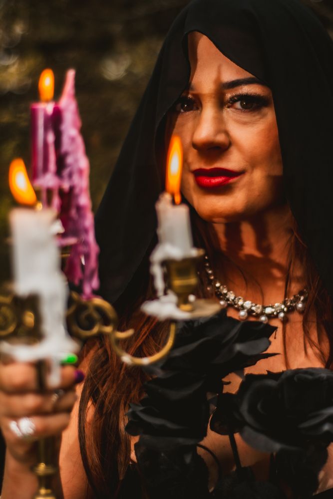 Closeup of hooded figure with candlelight illuminating silver necklace and red lips.