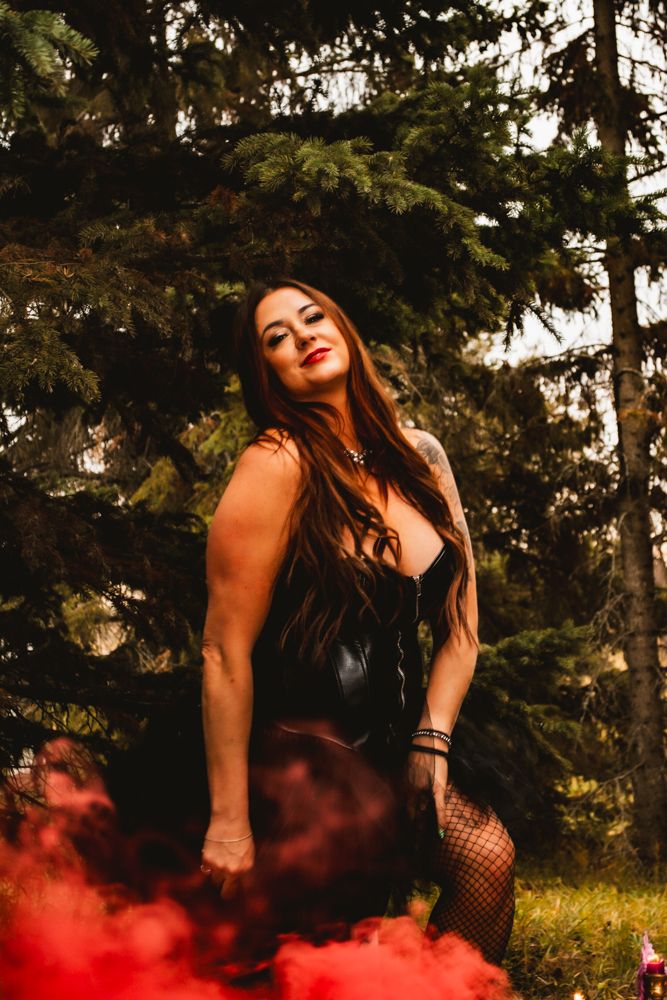 A dramatic portrait with red smoke effects captures gothic fashion in a forest environment.