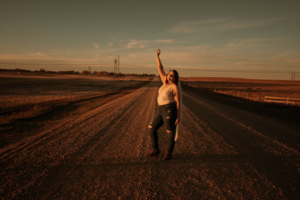 Silhouette of person with raised arm on rural road at sunset.