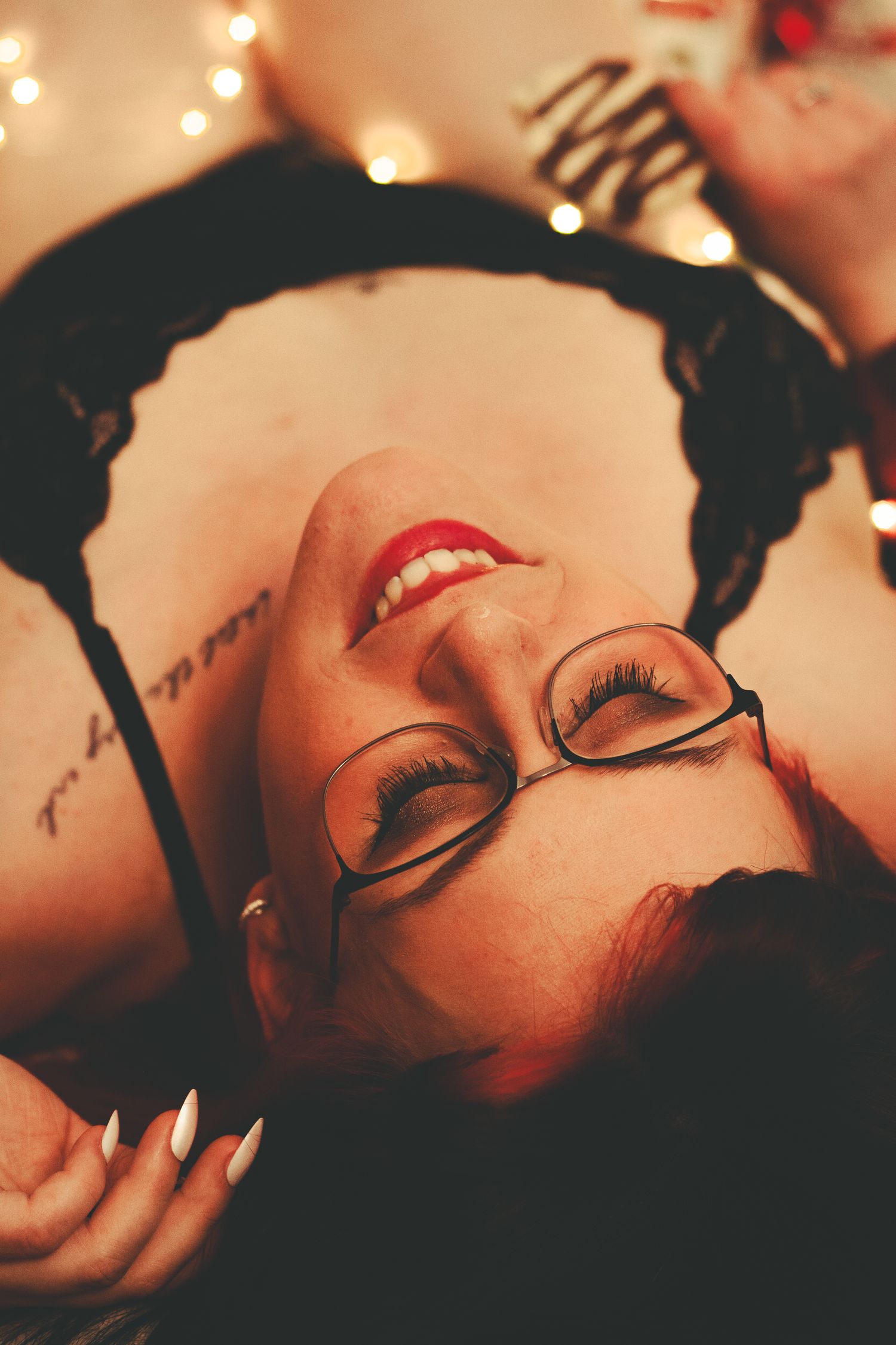 Close-up portrait with glasses and red lipstick against twinkling holiday lights.