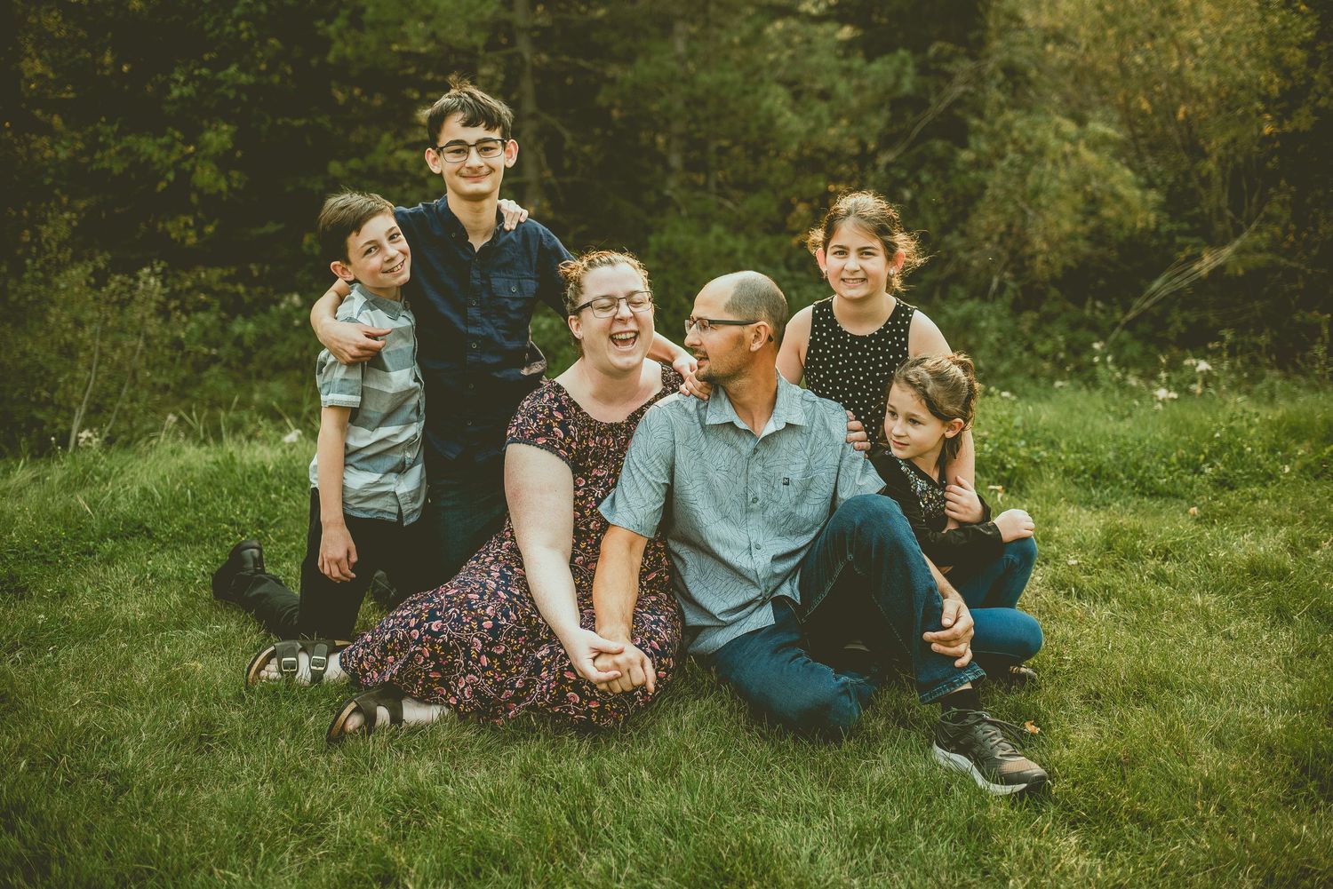 A family sits together on green grass in a casual outdoor portrait setting during summer.