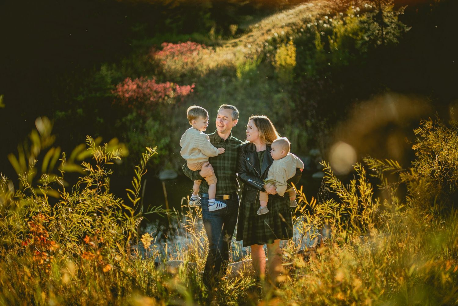 A couple shares a romantic moment in a golden sunlit meadow surrounded by wildflowers at sunset.