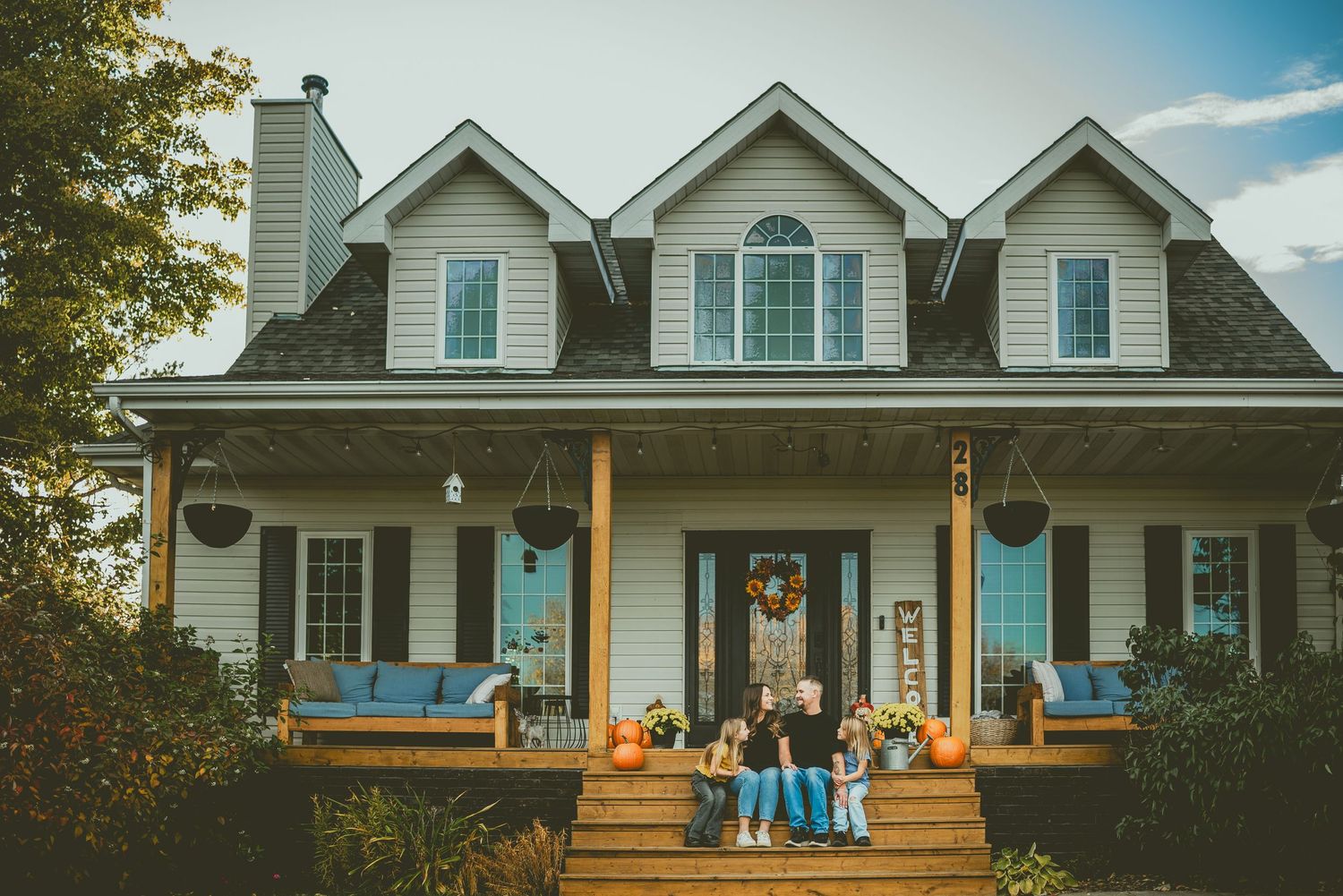 Family posing on the porch of a charming Cape Cod home decorated with fall pumpkins and autumn decor.