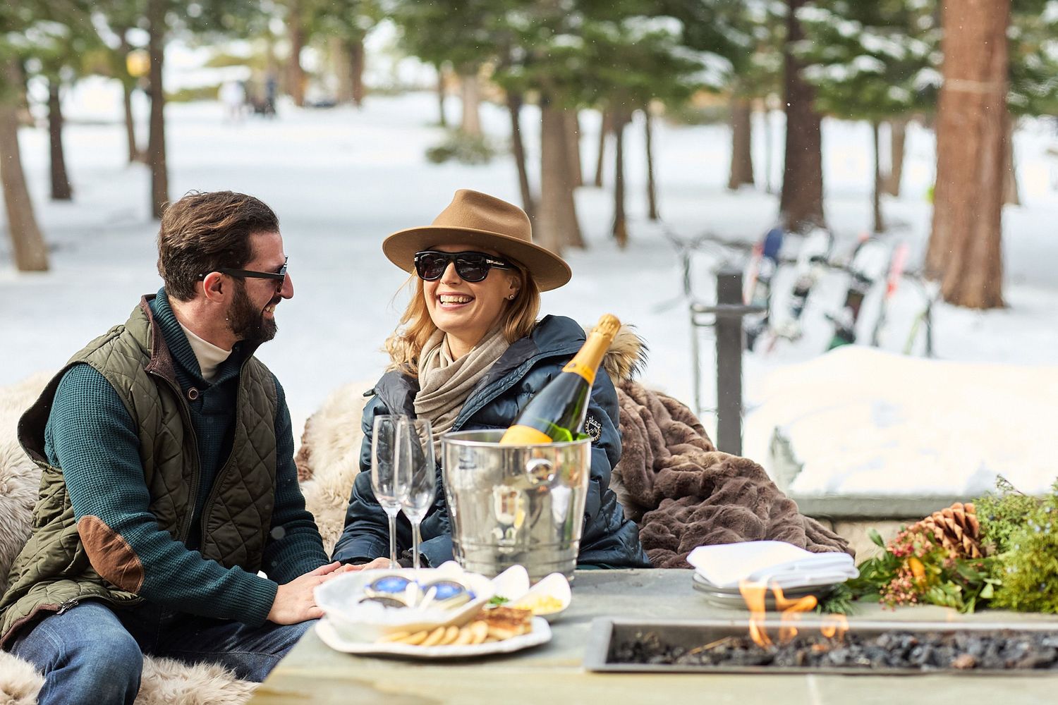 Couple enjoying a cozy winter meal outdoors at a snowy restaurant patio with heaters and warm blankets.