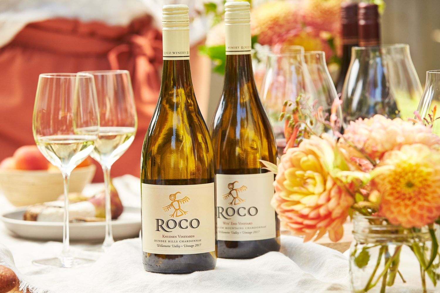 Wine bottles and glasses elegantly arranged with soft floral decorations.