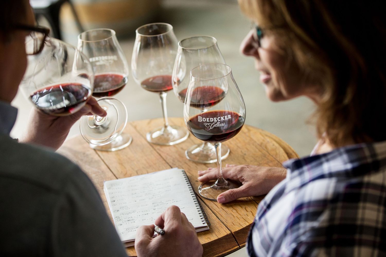 Wine tasting session with multiple glasses of red wine and tasting notes on wooden table.