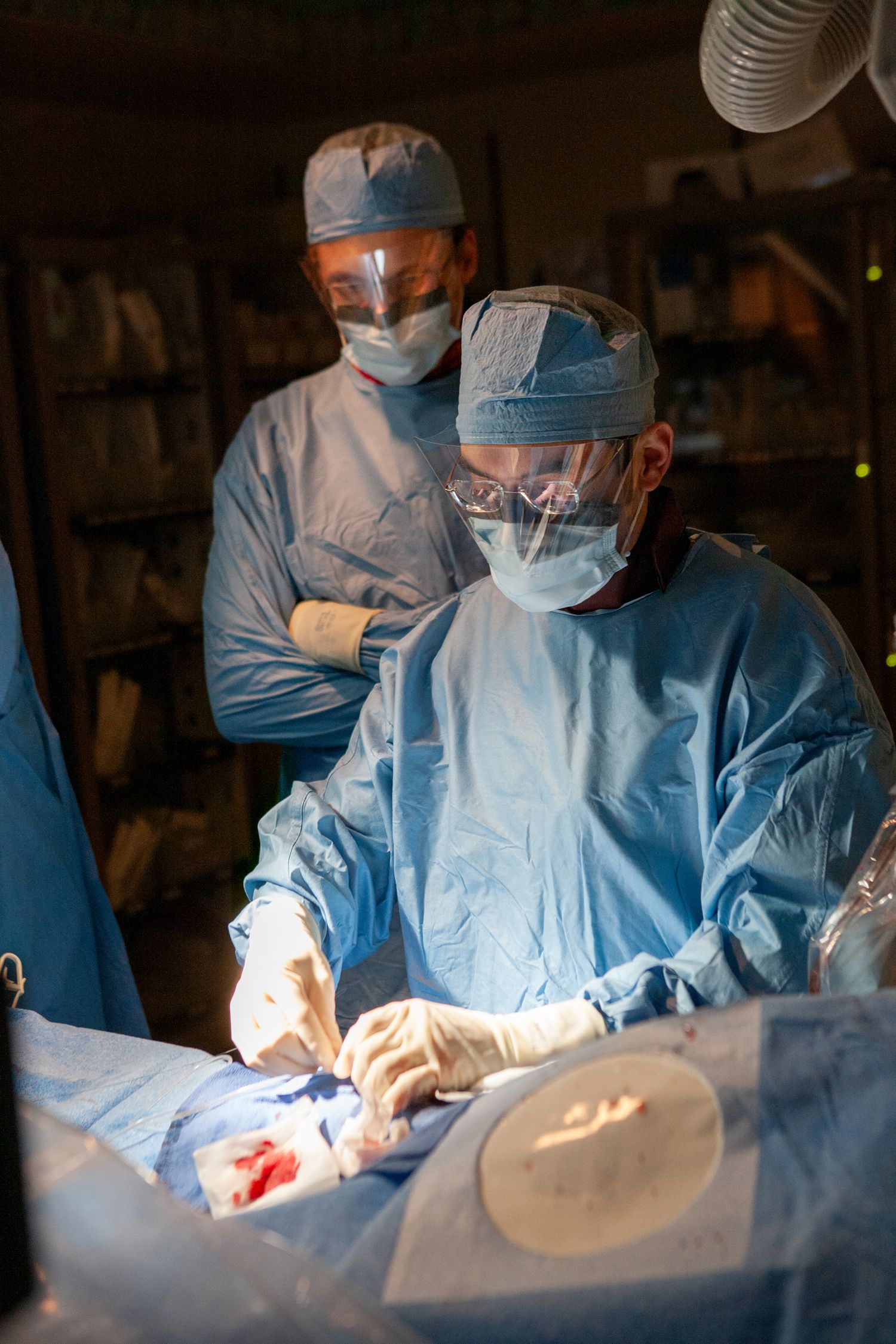 Medical team performing surgery in operating room wearing protective gear.