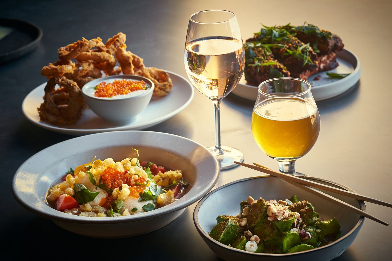 Restaurant table setting with plated dishes and drinks under warm lighting.