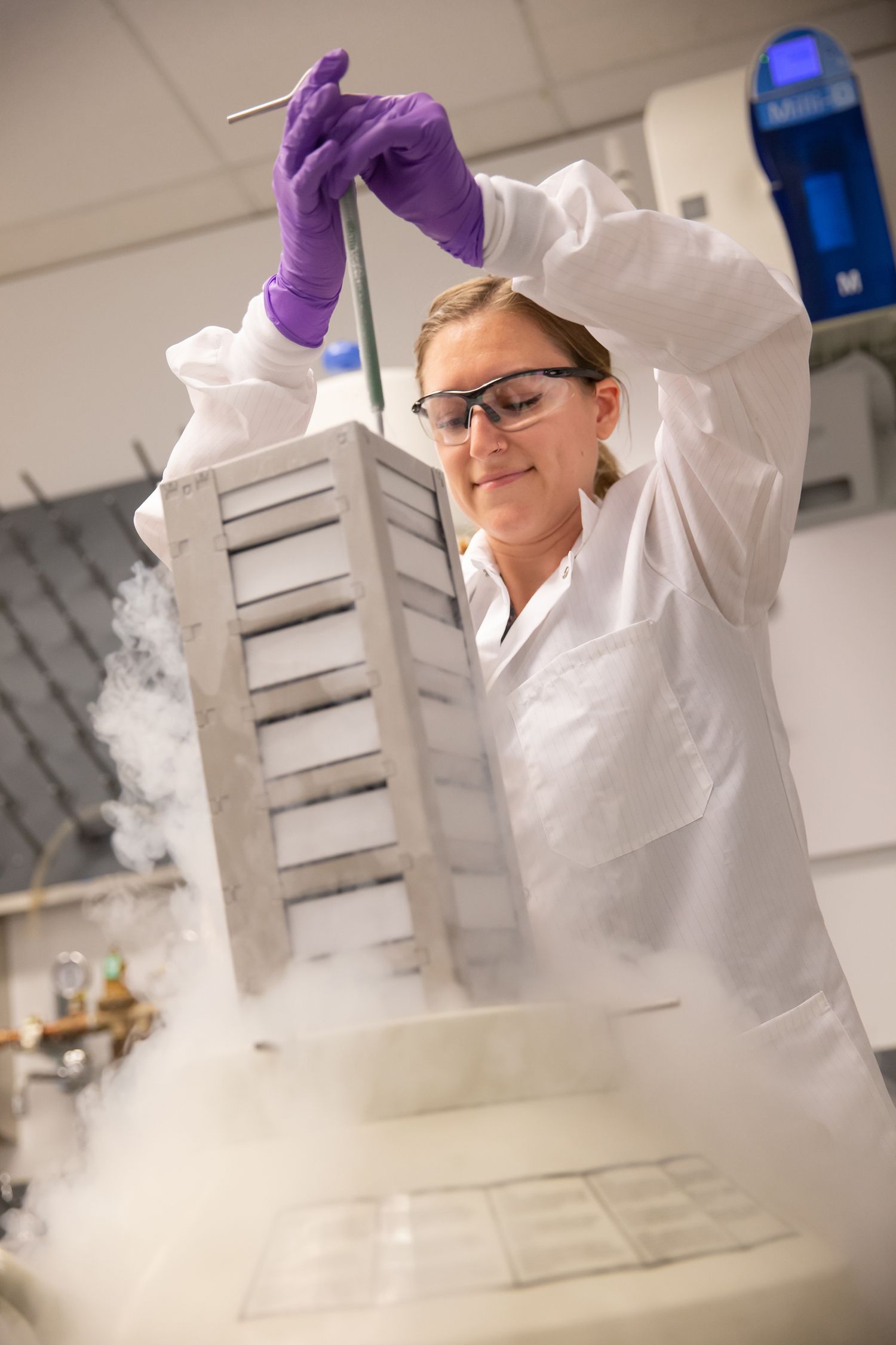 Laboratory technician in protective gear working with liquid nitrogen in scientific setting.